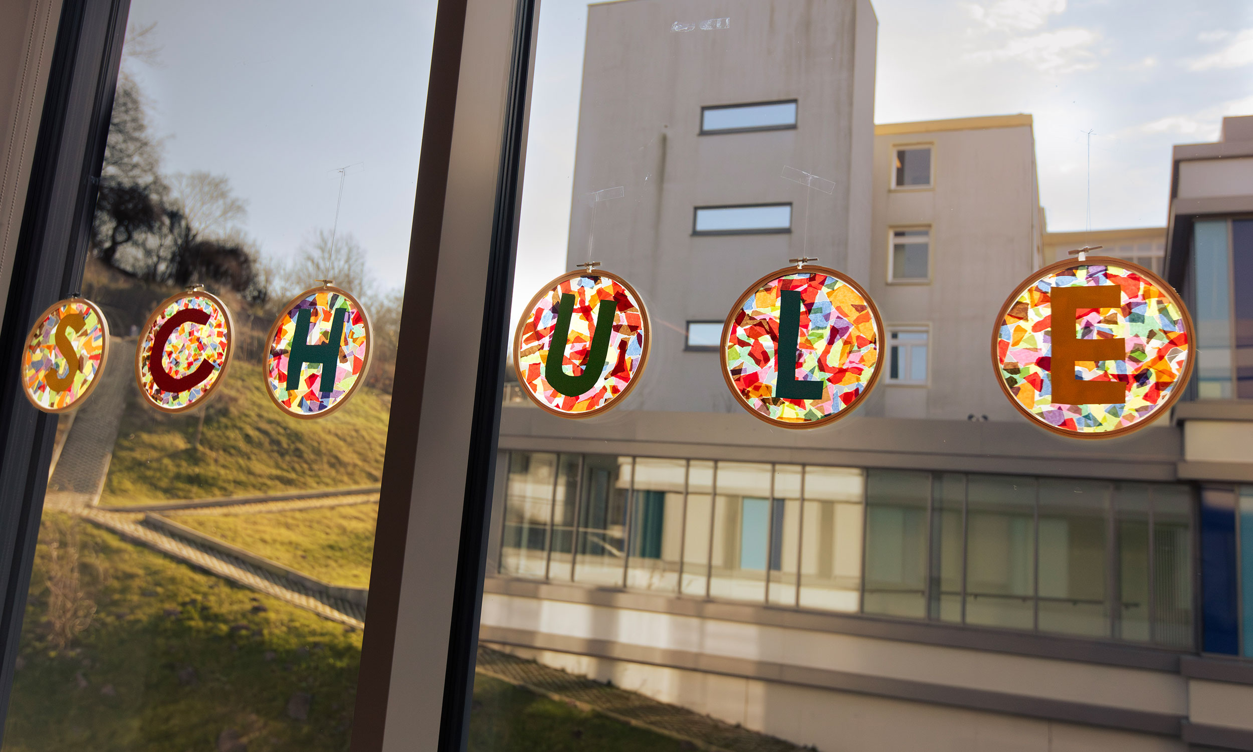 Blick aus dem Fenster der Dothanschule. In dem Fenster hngen halbtransparente gebastelte farbige Buchstaben die zusammen das Wort Schule bilden.